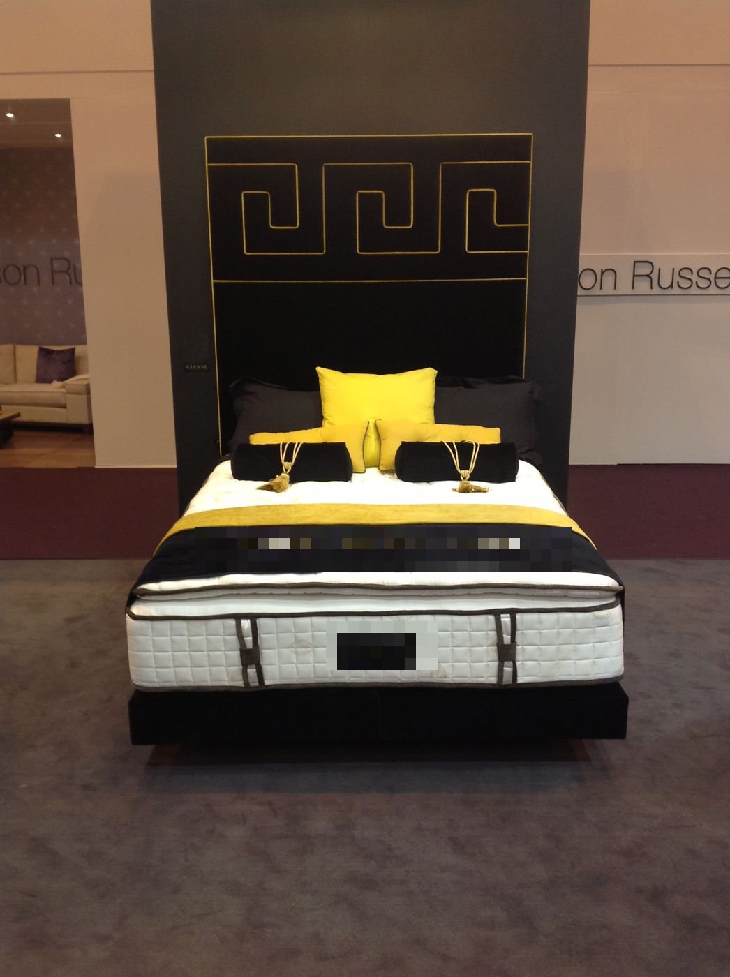 Royal Bohemia branded bed with black and gold headboard and mustard yellow cushions at a trade show