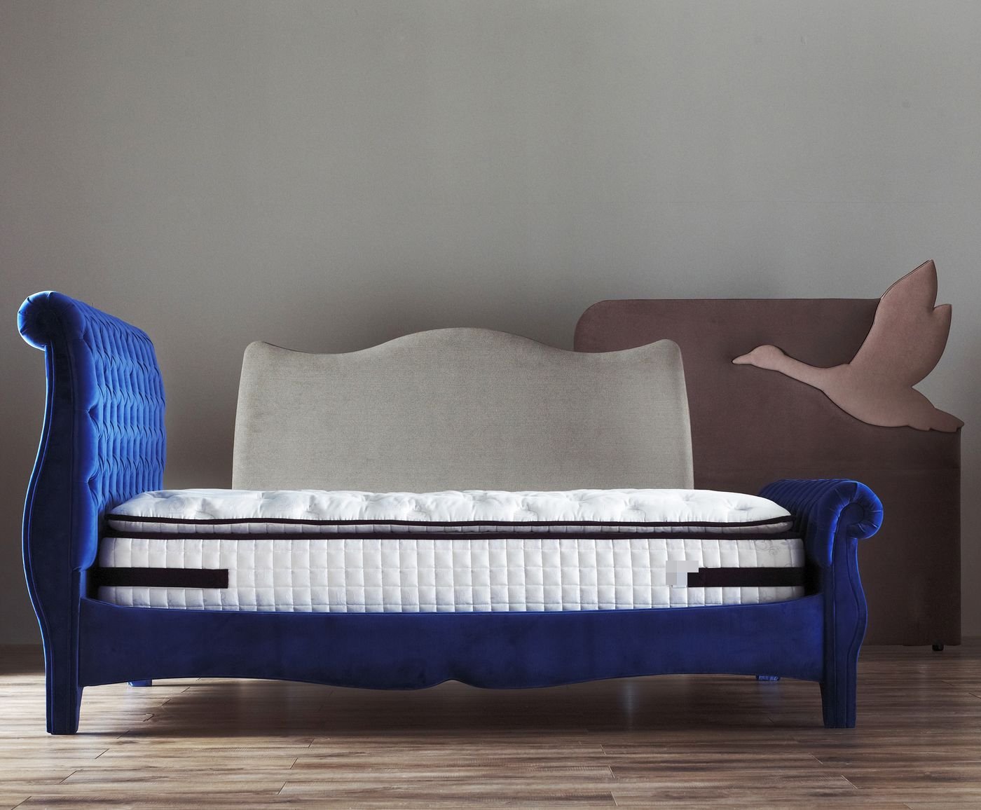 Studio lineup of three Royal Bohemia beds: blue tufted, grey camelback, and pink goose-wing headboards