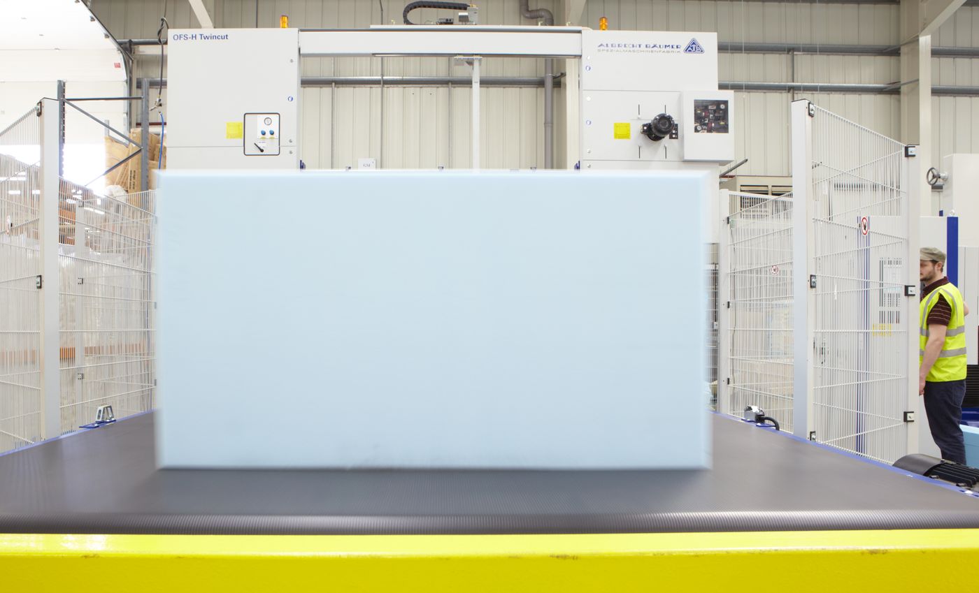 Factory worker in a hi-vis vest operating a Twincut CNC foam cutting machine with a pale blue foam block