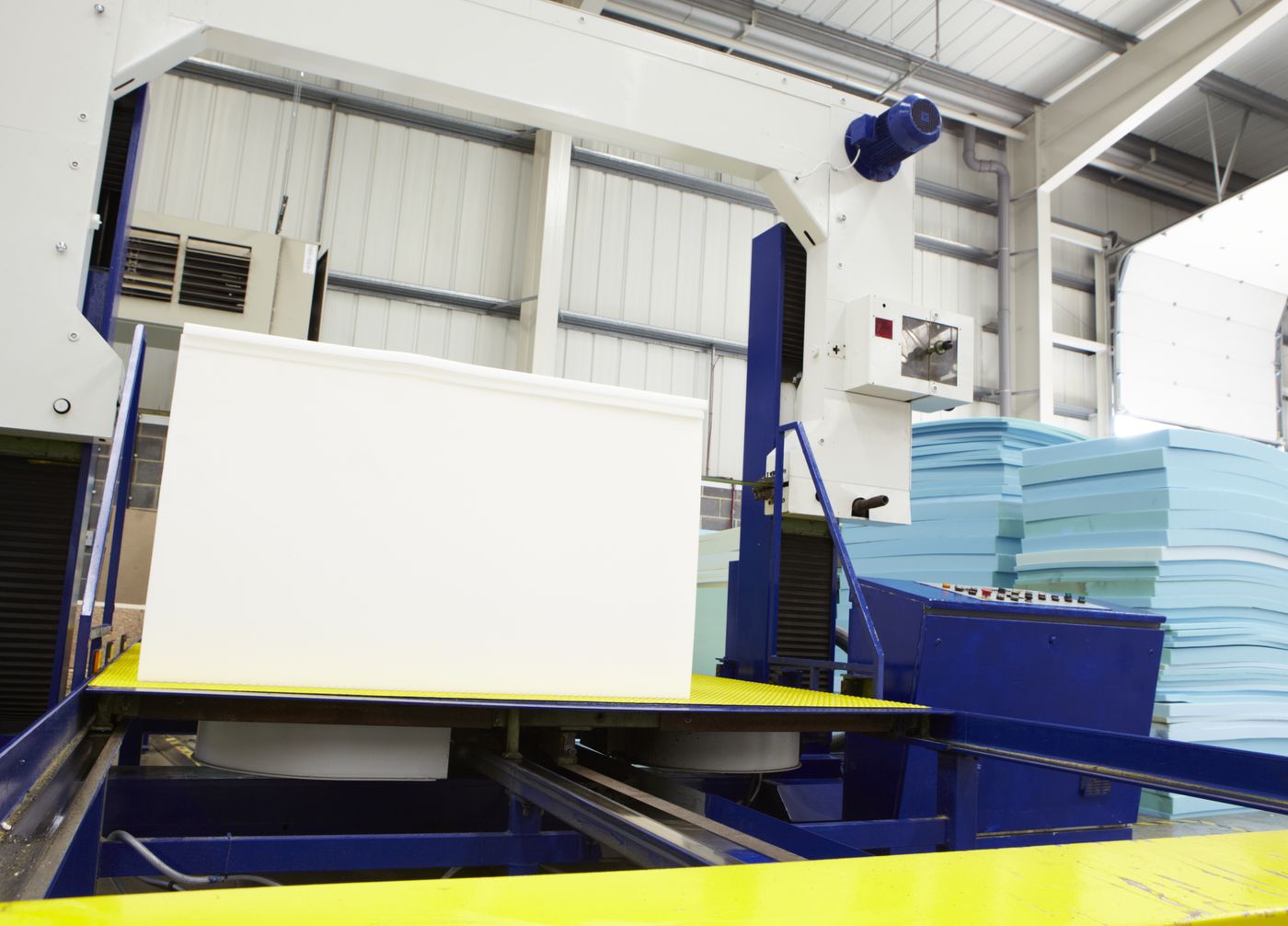 Foam block on a factory production line conveyor with stacked foam sheets in the background