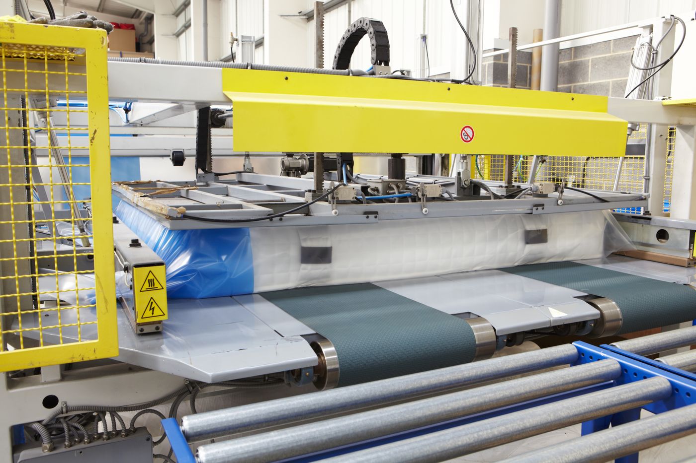Mattress being compressed and wrapped by a roll-packing machine on the factory floor