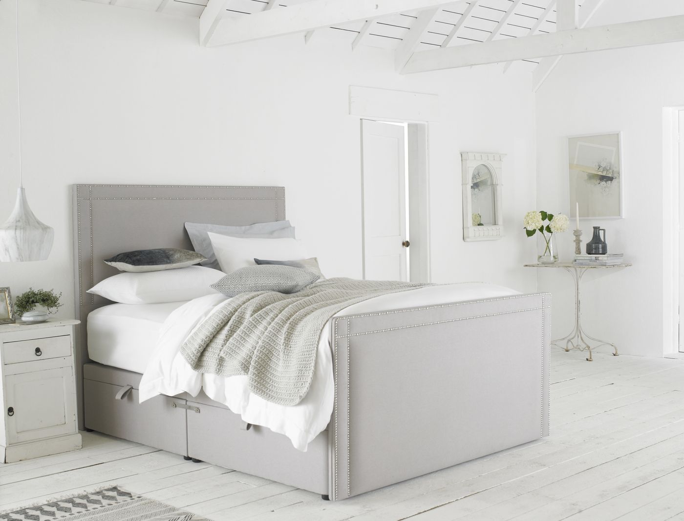 Charcoal upholstered headboard with silver nailhead trim styled in a bright bedroom with a herringbone floor