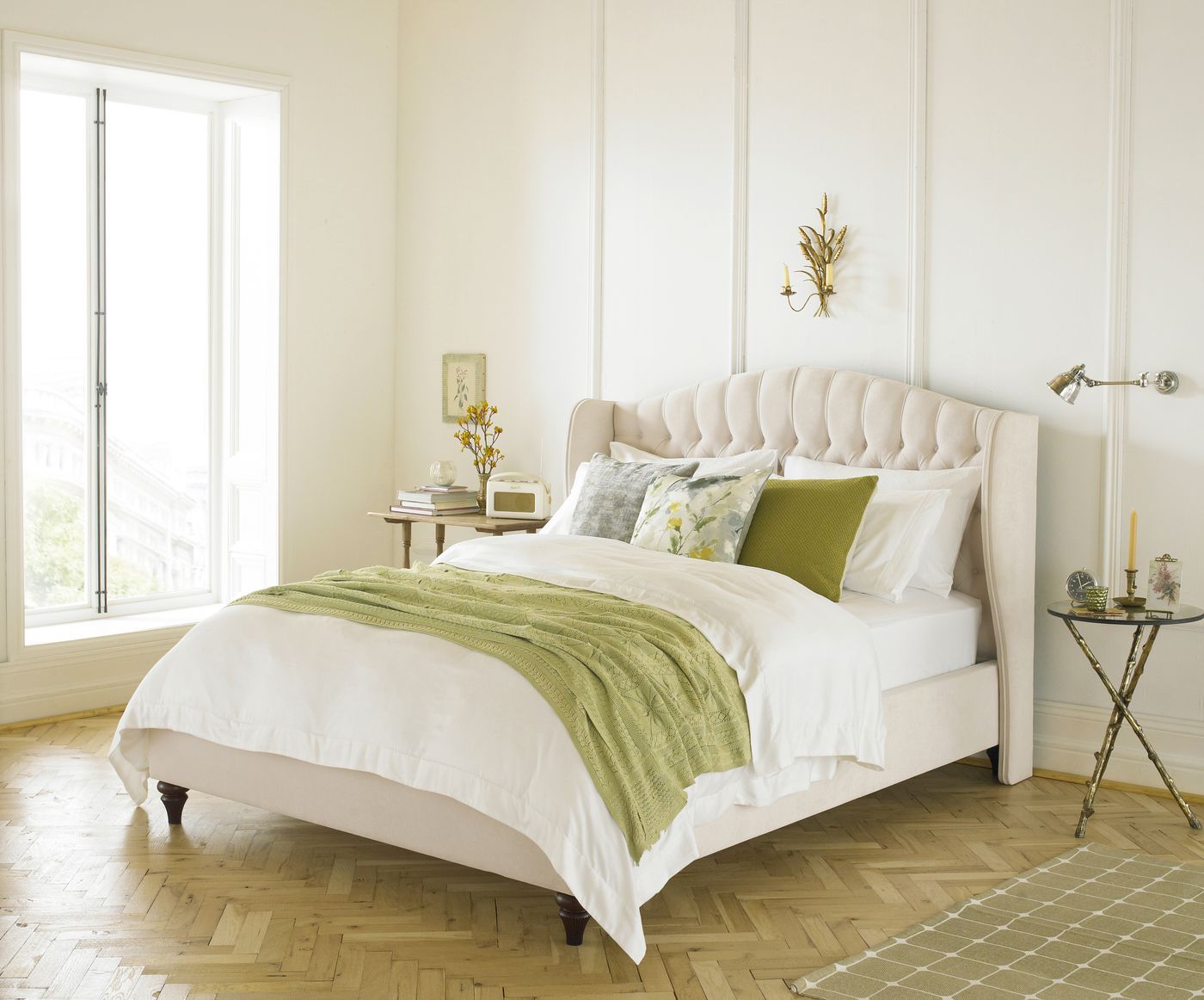 Cream button-tufted wingback bed styled in an elegant bedroom with a parquet floor and wall sconce