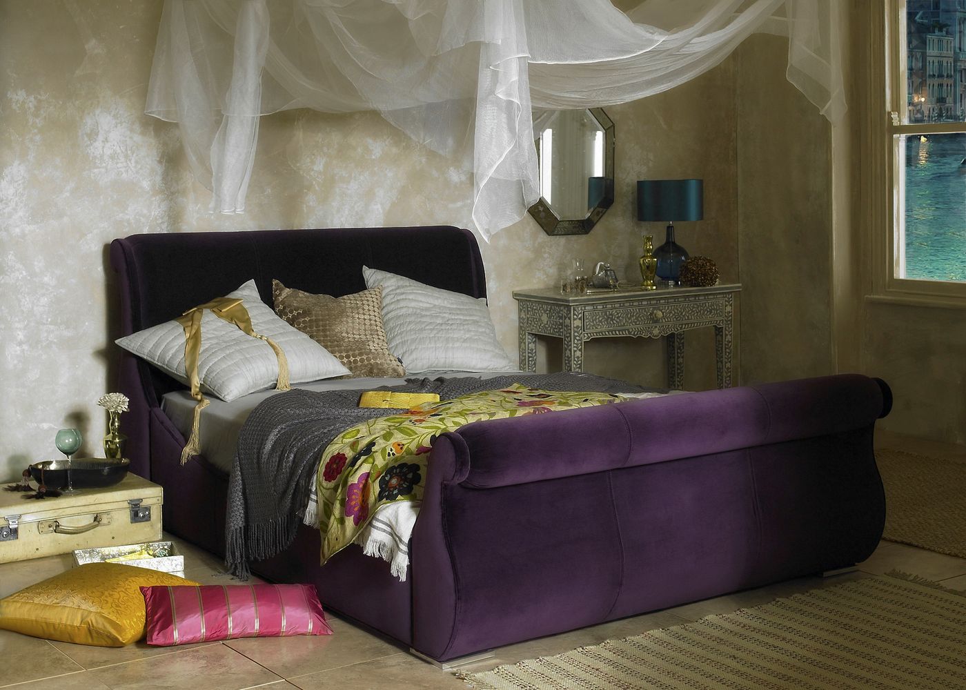 Purple velvet sleigh bed styled in an ornate bedroom with sheer canopy netting and a Venice view