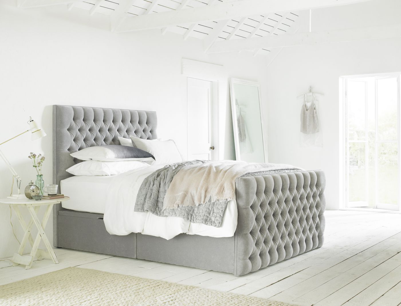 Grey button-tufted bed with storage base styled in a bright white loft bedroom