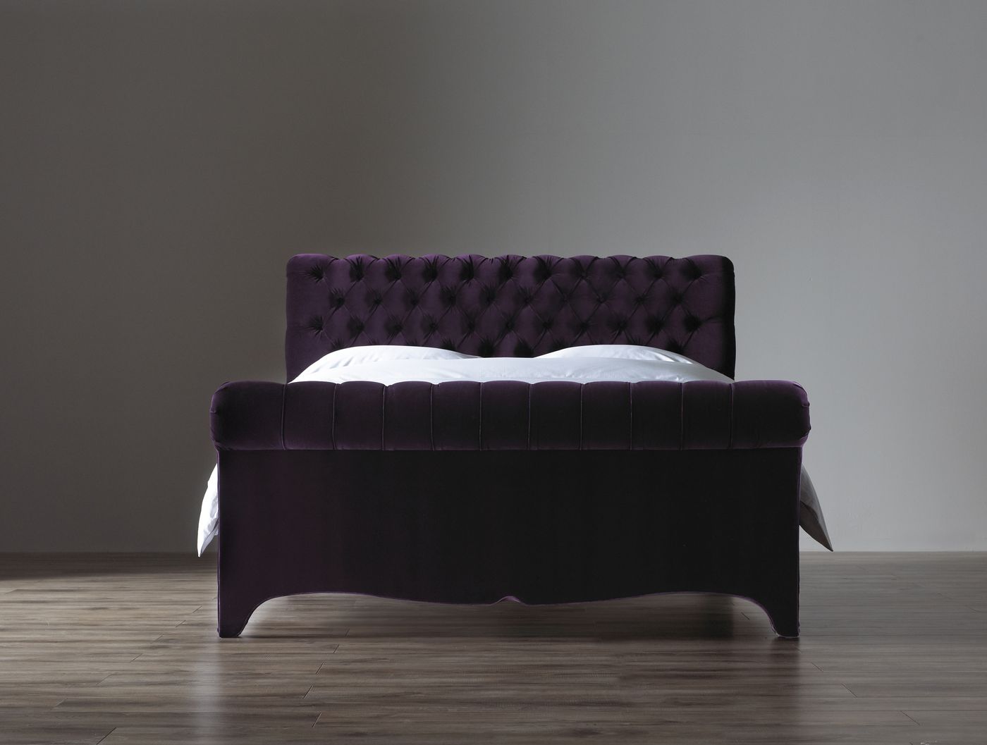Studio product photo of a deep purple velvet button-tufted bed frame with white bedding