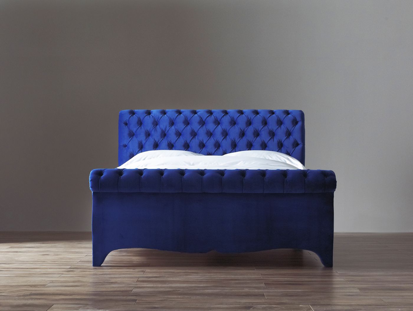 Studio product photo of a royal blue velvet button-tufted chesterfield-style bed frame
